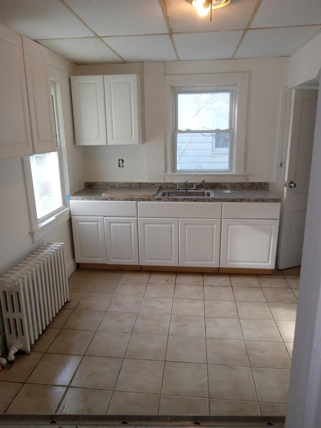 kitchen featuring a paneled ceiling, light tile patterned floors, white cabinets, and radiator heating unit