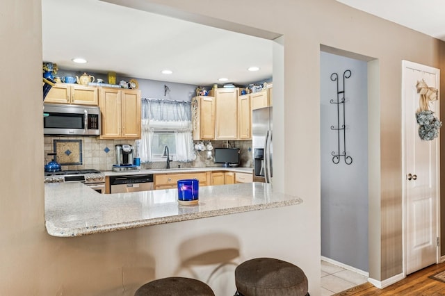 kitchen with light brown cabinetry, tasteful backsplash, a sink, a peninsula, and stainless steel appliances