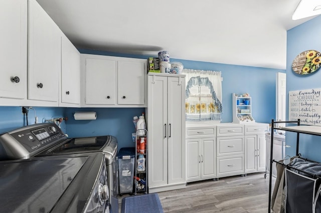clothes washing area with cabinet space, washer and clothes dryer, and light wood-style floors