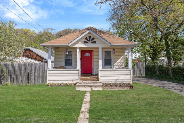 bungalow-style home with covered porch, fence, a shingled roof, and a front yard