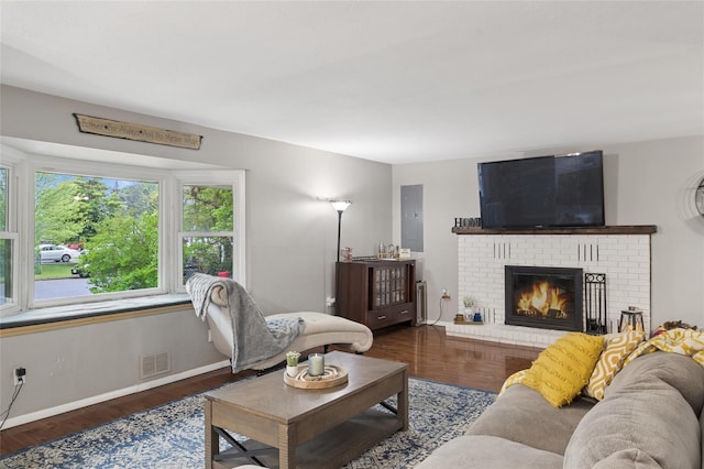 living area featuring a brick fireplace, wood finished floors, baseboards, and electric panel