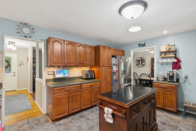 kitchen with stainless steel fridge with ice dispenser, dark countertops, decorative backsplash, brown cabinetry, and baseboards