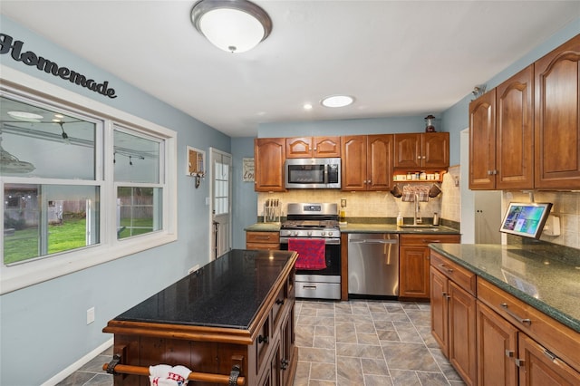 kitchen featuring appliances with stainless steel finishes, tasteful backsplash, brown cabinets, a sink, and baseboards