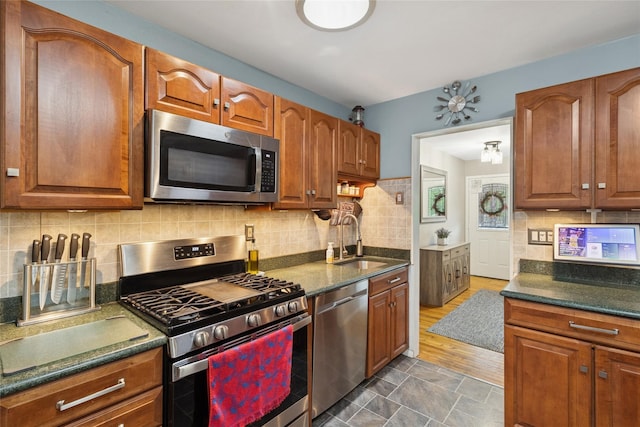 kitchen featuring appliances with stainless steel finishes, a sink, tasteful backsplash, and brown cabinets