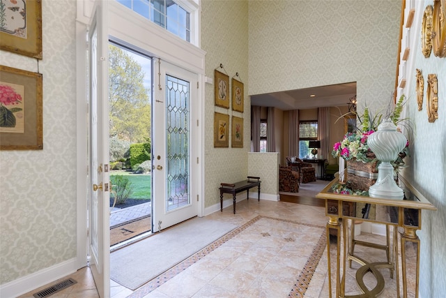entrance foyer featuring wallpapered walls, visible vents, baseboards, and a high ceiling