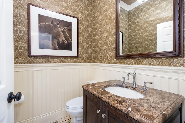 bathroom with vanity, toilet, wallpapered walls, and a wainscoted wall