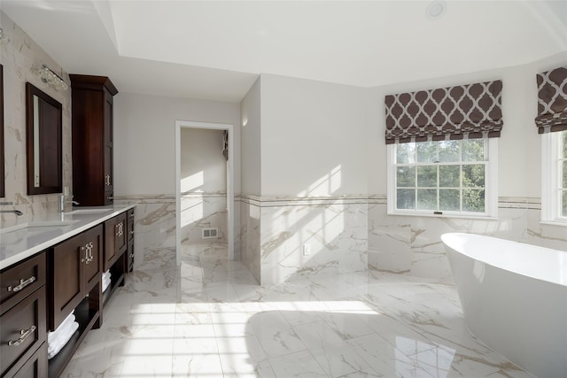 bathroom with a sink, tile walls, a soaking tub, and a wainscoted wall