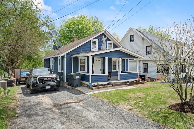 bungalow-style home featuring covered porch, driveway, a chimney, a front yard, and central AC