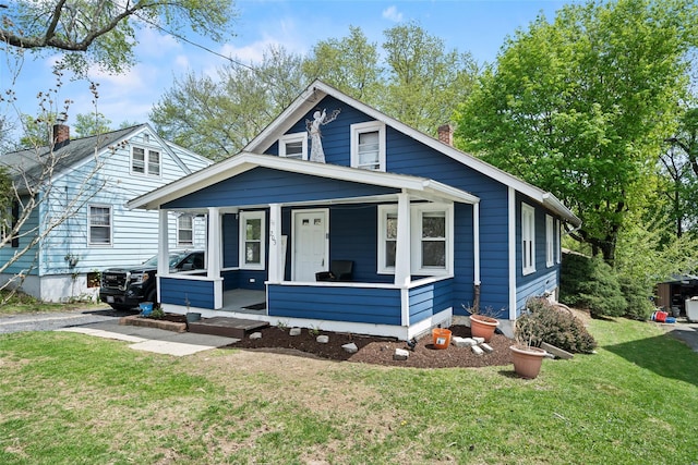 bungalow-style home with a porch, a chimney, and a front lawn