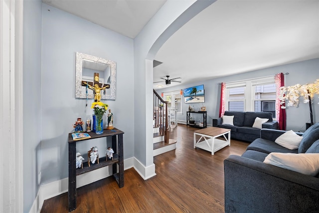 living room featuring arched walkways, a ceiling fan, baseboards, wood finished floors, and stairway