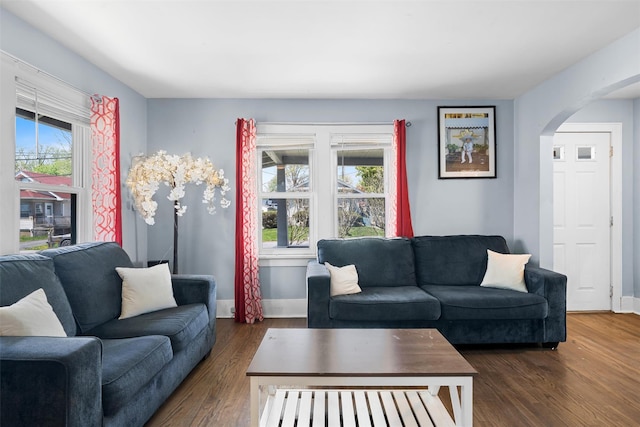 living area featuring baseboards, arched walkways, and dark wood finished floors