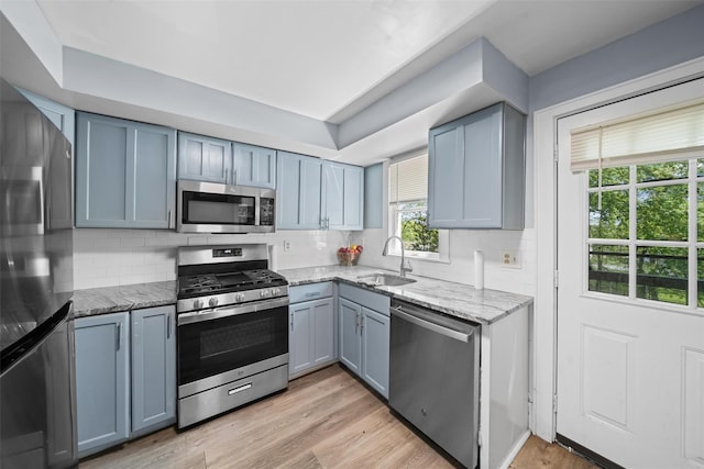 kitchen with light stone counters, a sink, decorative backsplash, and appliances with stainless steel finishes