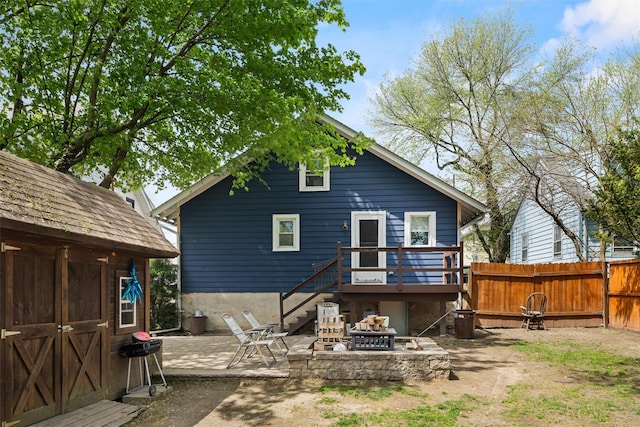 rear view of property featuring fence, a wooden deck, a patio, an outdoor fire pit, and an outbuilding
