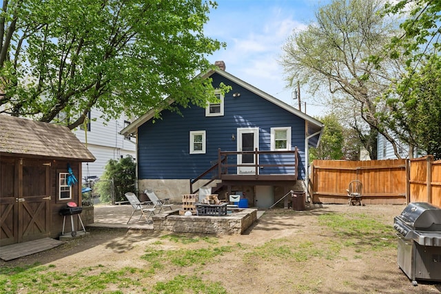 back of house featuring an outdoor structure, fence, a deck, a chimney, and an outdoor fire pit