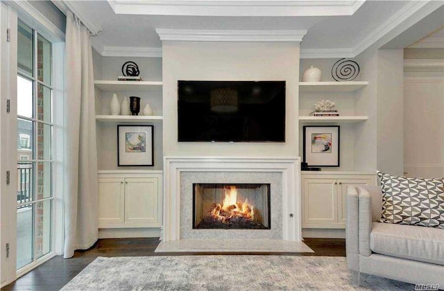 living room with crown molding, built in features, a lit fireplace, and dark wood-style flooring