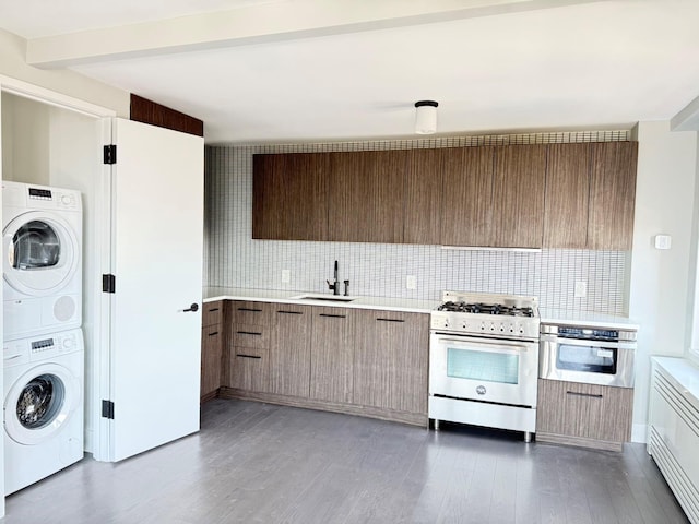 kitchen featuring decorative backsplash, appliances with stainless steel finishes, a sink, light countertops, and stacked washer and clothes dryer