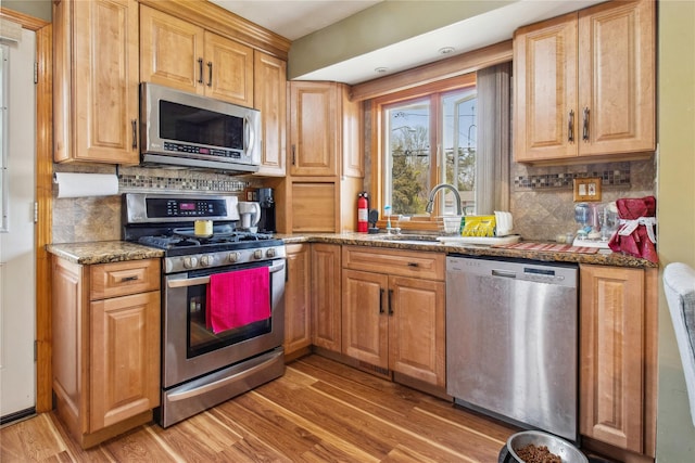 kitchen with light stone countertops, appliances with stainless steel finishes, a sink, light wood finished floors, and backsplash