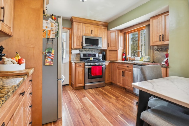 kitchen with light stone counters, appliances with stainless steel finishes, a sink, light wood finished floors, and tasteful backsplash