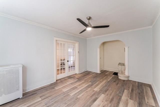unfurnished room featuring a ceiling fan, arched walkways, wood finished floors, and radiator