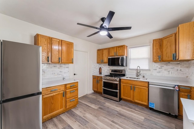 kitchen with a sink, light countertops, stainless steel appliances, a ceiling fan, and decorative backsplash