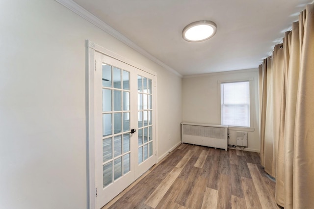 empty room with french doors, crown molding, wood finished floors, baseboards, and radiator heating unit