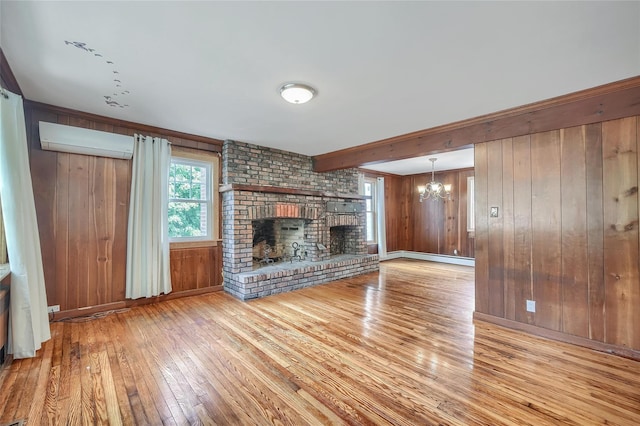 unfurnished living room with a fireplace, hardwood / wood-style floors, a wall mounted air conditioner, wooden walls, and a chandelier
