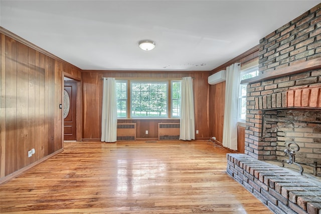 unfurnished living room featuring wood walls, radiator, light wood finished floors, and a wall unit AC