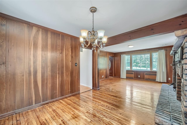unfurnished living room featuring wood walls, radiator heating unit, a notable chandelier, and hardwood / wood-style flooring