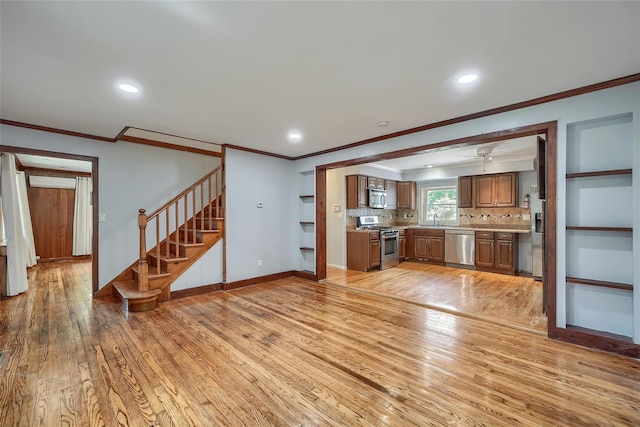 unfurnished living room featuring crown molding, a ceiling fan, stairs, and light wood-type flooring