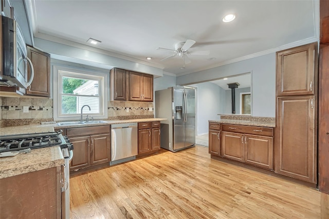 kitchen featuring ceiling fan, ornamental molding, stainless steel appliances, and light wood-style flooring