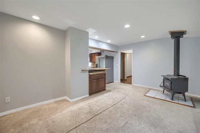 unfurnished living room featuring baseboards, a wood stove, recessed lighting, and light colored carpet