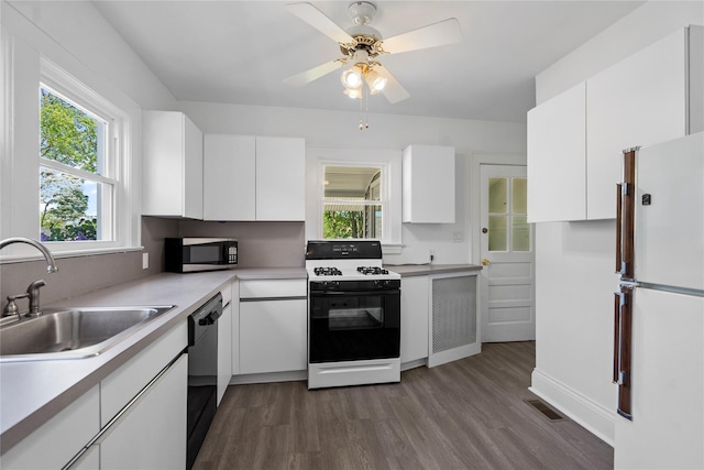 kitchen featuring white cabinets, a sink, freestanding refrigerator, stainless steel microwave, and gas range oven