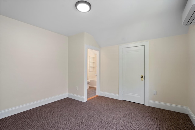 empty room with dark colored carpet, baseboards, a wall unit AC, and vaulted ceiling