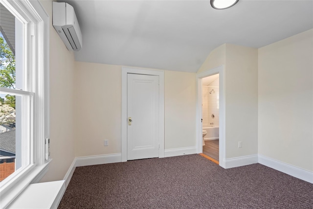 unfurnished bedroom with connected bathroom, carpet floors, baseboards, a wall unit AC, and vaulted ceiling