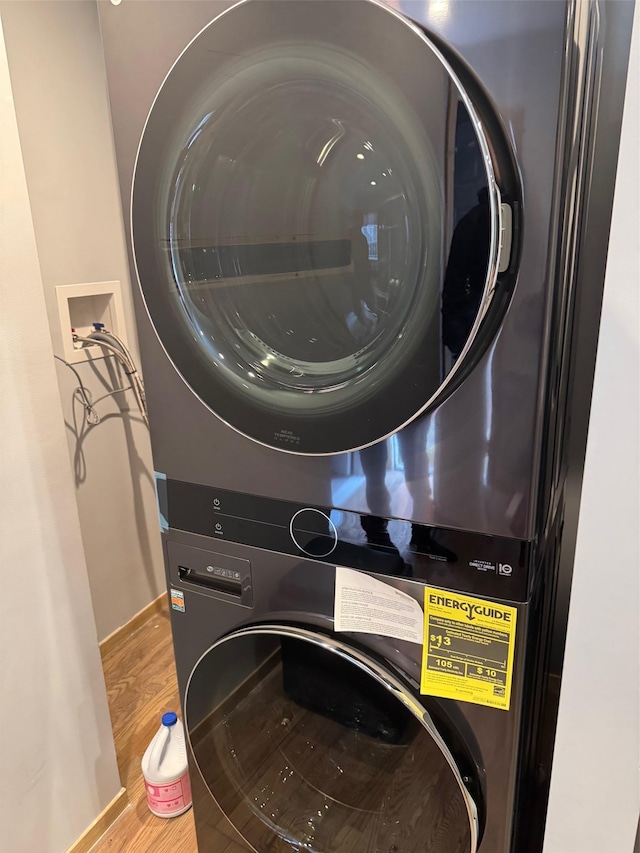 laundry room with baseboards, stacked washer / drying machine, wood finished floors, and laundry area