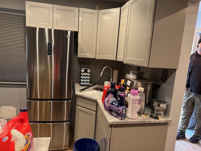 kitchen featuring freestanding refrigerator, wood finished floors, white cabinetry, light stone counters, and a sink