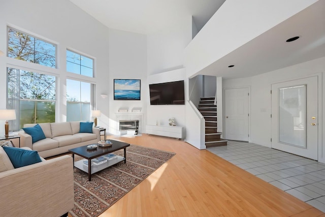 living area with stairs, a glass covered fireplace, wood finished floors, and a towering ceiling