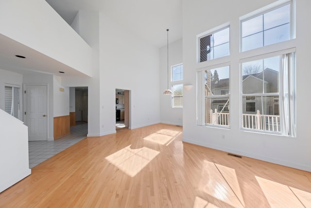 unfurnished living room featuring a high ceiling, visible vents, plenty of natural light, and light wood-type flooring