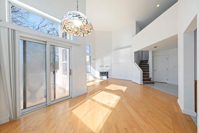 unfurnished living room with a towering ceiling, light wood-type flooring, stairway, baseboards, and a glass covered fireplace