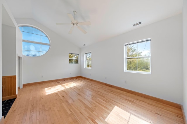 empty room featuring visible vents, a wealth of natural light, vaulted ceiling, and light wood-style floors