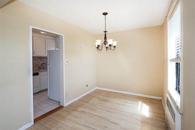 unfurnished dining area featuring a sink, baseboards, light wood-type flooring, and a chandelier