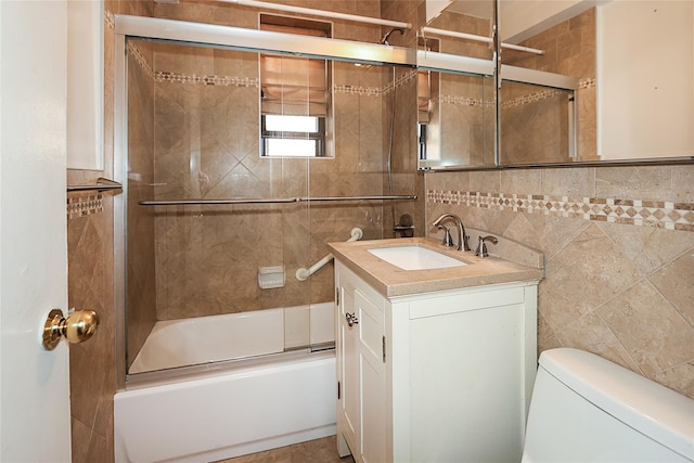 full bathroom with tile walls, bath / shower combo with glass door, vanity, and toilet