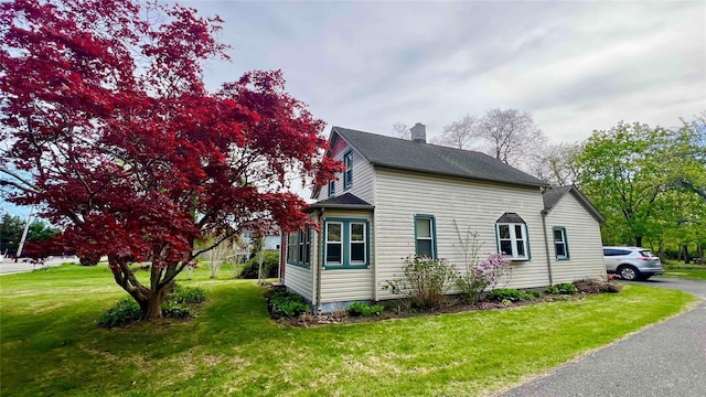 view of home's exterior with a lawn, a chimney, and roof with shingles