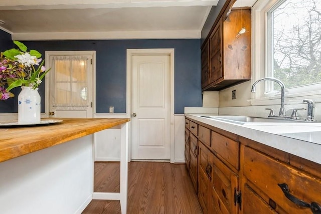 kitchen featuring a sink, wood counters, brown cabinetry, baseboards, and dark wood-type flooring