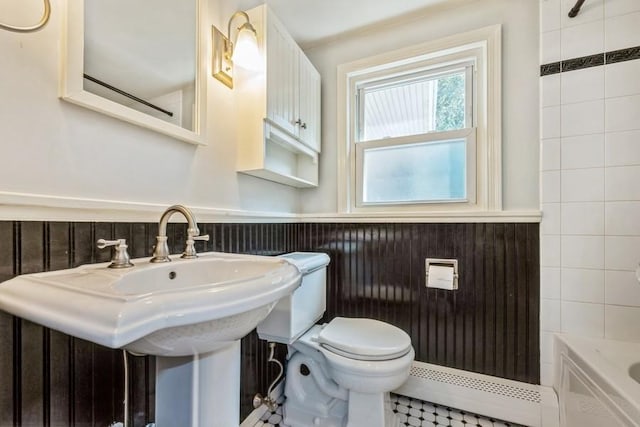 full bath with baseboard heating, wainscoting, a sink, toilet, and bathing tub / shower combination