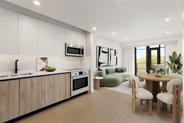 kitchen with light wood-style floors, wall oven, modern cabinets, stainless steel microwave, and a sink