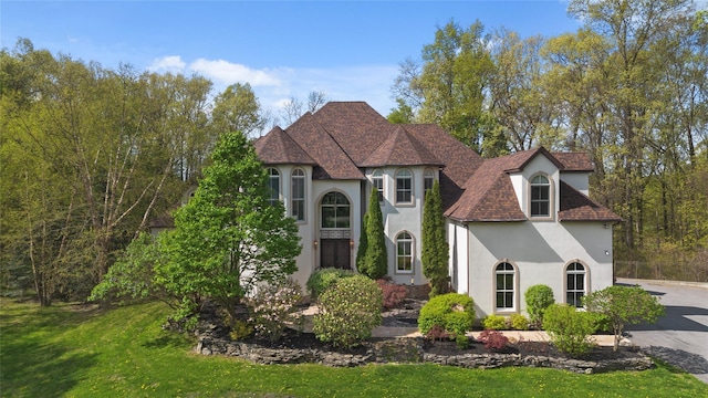 french country style house featuring a shingled roof, a front yard, and stucco siding