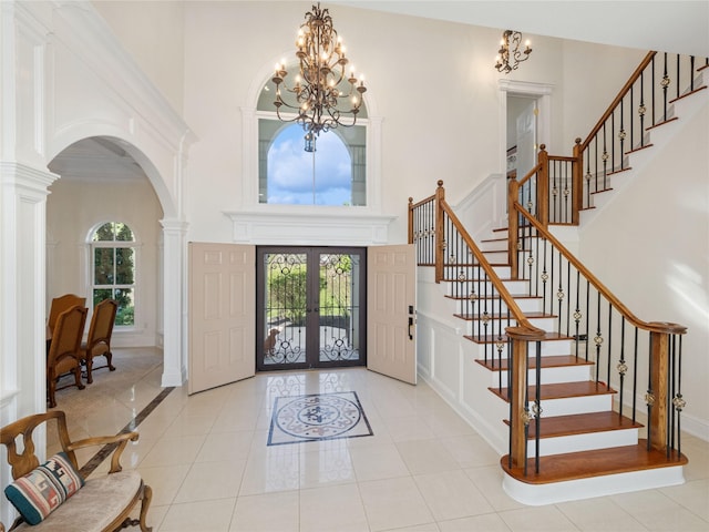 entryway featuring french doors, a towering ceiling, arched walkways, stairway, and an inviting chandelier