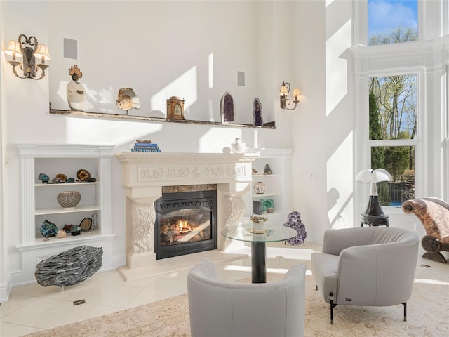 living area featuring a premium fireplace, tile patterned floors, built in shelves, and a towering ceiling