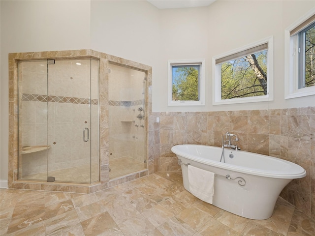 bathroom featuring wainscoting, marble finish floor, a freestanding tub, tile walls, and a stall shower